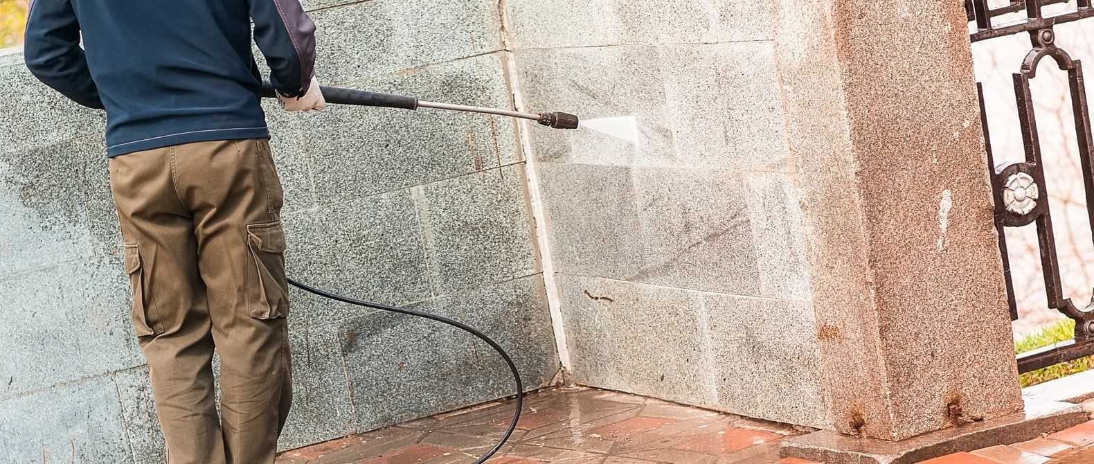 Arbeiter reinigt Mauer mit Hochdruckstrahler.