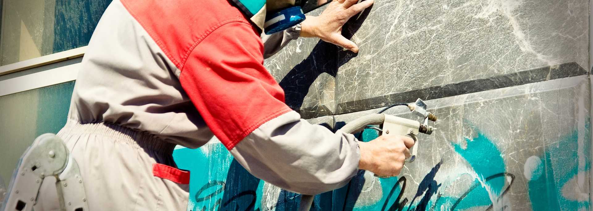 Arbeiter in Schutzanzug entfernt mit mit Hochdruck Grafitti auf Hauswand.
